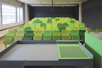 Hörsaal mit Pult für den Lehrenden und grüner Bestuhlung