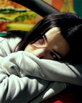 Zu sehen ist ein junge Frau auf einem Stuhl. Hintergrund ist Bunt.