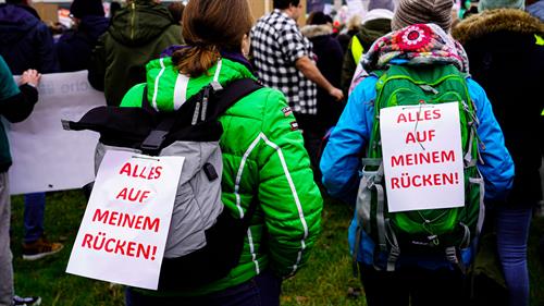 Demonstrierende Studierende mit einem Poster auf dem Rücken, auf dem Steht: "Alles auf meinem Rücken!"