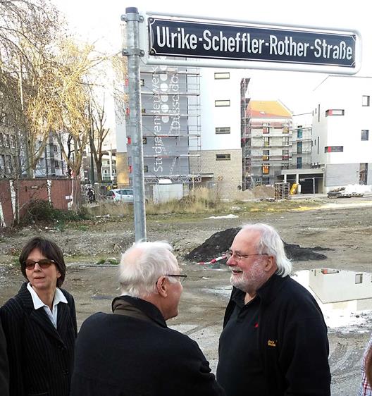 Straßenschild "Ulrike-Scheffler-Rother-Straße" mit drei Menschen im Vordergrund und einer Baustelle im Hintergrund