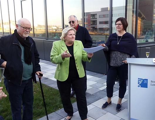 Zwei Männer und zwei Frauen, eine Frau mit hellgrünen Jacket hält eine Rede