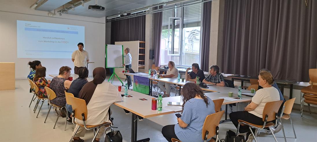 Personen sitzen an einer U-förmigen Tischformation und schauen den Sprecher in der Mitte an.