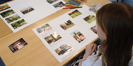 Kind an einem Tisch mit beschrifteten Fotos und Buntstiften