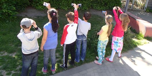Vier Kinder von Hinten mit Fotoapparaten auf einer Wiese.