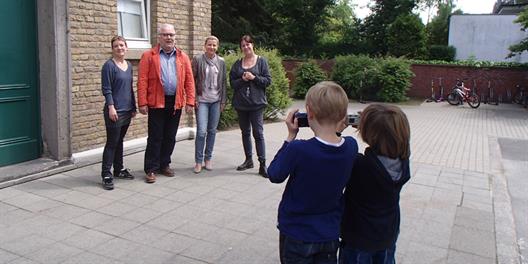Zwei Kinder fotografieren vier Erwachsene auf einem Schulhof