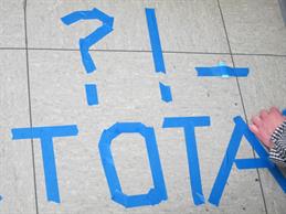 Auf dem Boden eines Raumes wurde mit blauem Klebenand folgende Symbole bzw. Wortstücke geschreiben: ?! TOTA