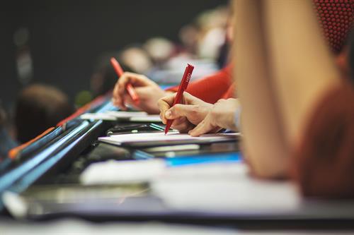 Hände von Studierende in einem Hörsaal schreiben mit einem HSD-Kuli