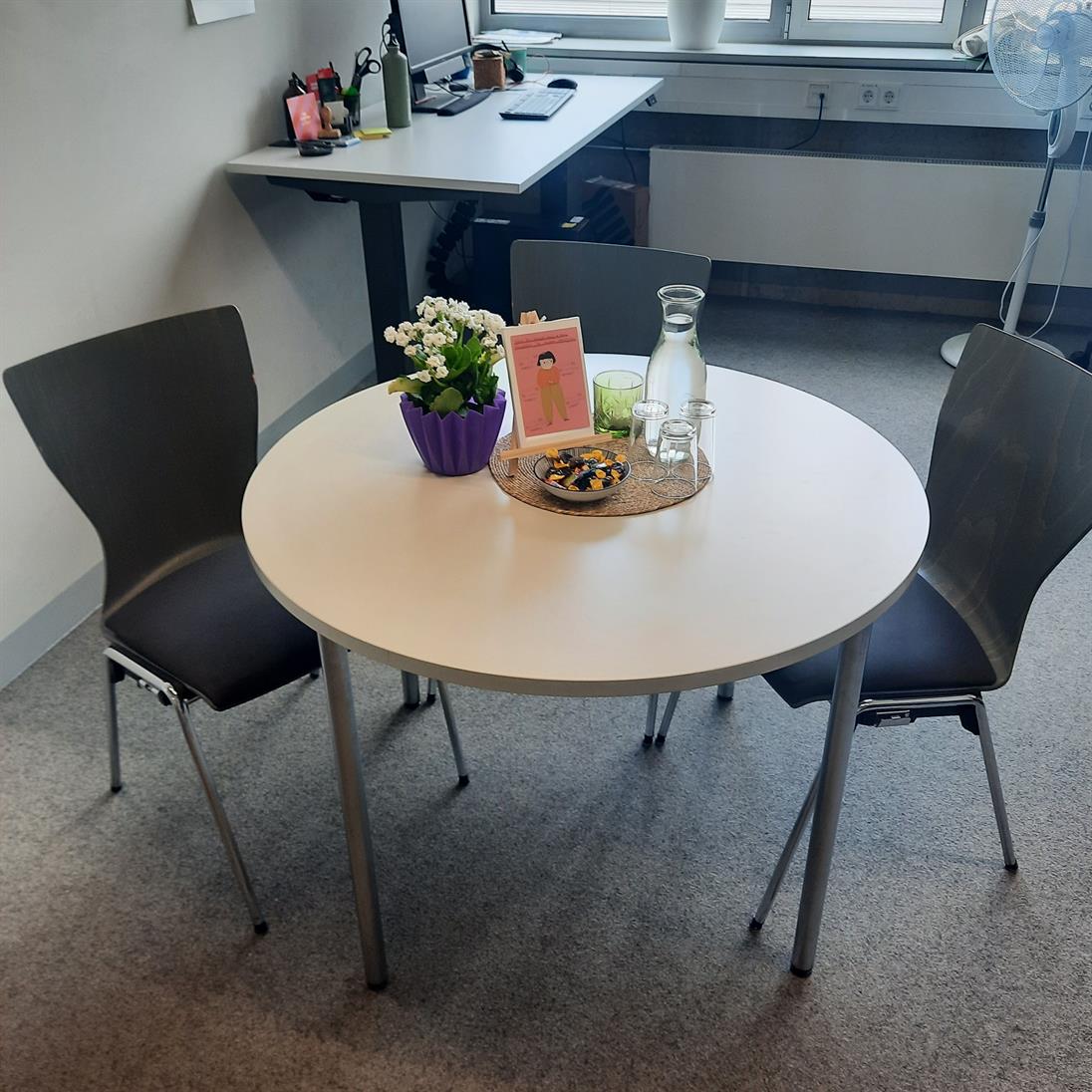 Runder Beratungstisch im Büro des Praxisreferats. Es gibt 3 Stühle und einen Platz für einen Rollstuhl an dem Tisch. 